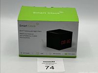 Closed retail box of the Smart Clock showing the product image, green and white packaging, and key features including WiFi camera with night vision and built-in battery.