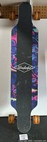 Top view of longboard showing black grip tape with 'Some Kind Of Wonderful' logo and colorful marbled design on edges.