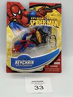 Front view of Spider-Man keychain in original blister packaging with clear plastic cover, showing Spider-Man figure attached to black web-shaped Spider-Sense device with keyring.