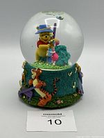Front and side view showing the Winnie-the-Pooh snow globe with Pooh holding Piglet inside the globe and Tigger, Eeyore figures at base