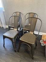 Four metal industrial style dining chairs grouped together, showing front and angled backrests, perforated metal seats, and curved tubular design.