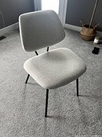 View of cream padded boucle desk chair angled showing padded seat, backrest and black metal legs.