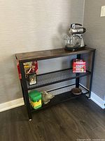 Hall table shown from a slight angle highlighting wooden top and mesh lower shelves with kitchen items