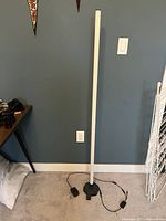 Tall white LED floor lamp standing upright with base and power cord visible, lamp turned off.