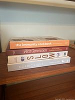 Side view of four cookbooks stacked: The Immunity Cookbook, First Generation, Slow, Nordic Light.