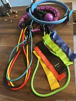 Blue Pilates ring with black grips, multi-colored loop resistance bands, and long resistance bands with handles all placed on wooden surface