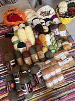 Overview of assorted yarn skeins and balls on a multicolored rug. Includes multiple colors and fiber types with some labels visible.