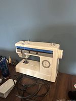 Front and side view of the vintage Brother sewing machine on a wooden surface, showing stitching settings and manual controls.