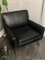 Front-left angle view of the black vinyl armchair, showing overall profile and armrest shape.