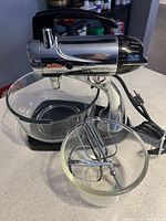 Sunbeam vintage stand mixer with one glass bowl and two metal beaters in smaller glass bowl, power cord visible.