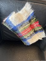Vintage tartan mohair scarf with visible frayed fringed edges, laid over black leather chair showing pattern and texture.