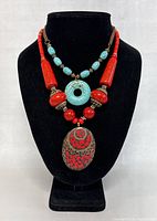 Necklaces and bracelet displayed on black bust showing red and turquoise beaded necklace with large circular turquoise pendant and oval red pendant.
