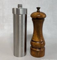 Two pepper grinders side by side, one stainless steel and one wooden, on a white background.