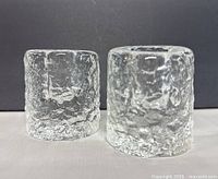 Front view of the two textured glass cylindrical candle holders, showing their rough clear glass surface and shape.