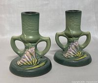 Pair of green glazed double handled Roseville Pottery candlesticks, front view showing floral design and shape