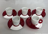 Five white ceramic espresso cups on half red/white saucers, arranged in a line showing full set