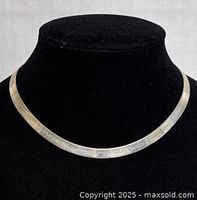 Flat choker necklace displayed on black mannequin bust showing front view of the silver chain with its texture and shine.