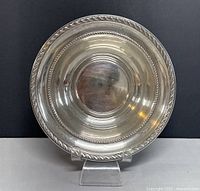 Front view of round sterling silver bowl with rope edge design on a stand.