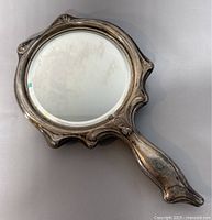 Front view of the hand held mirror showing smooth rounded edges and reflective surface in an ornate silver-toned frame.
