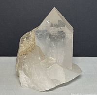 Clear quartz crystal showing pointed hexagonal prism with transparent and cloudy areas and attached rough matrix base.