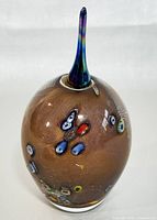 Side view of the brown oval glass perfume bottle with embedded millefiori accents and iridescent stopper in place.