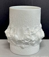 Front side view of the white ceramic vase showing the raised shell designs and textured surface.