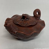 Side view of reddish-brown clay miniature teapot shaped like a leaf with frog figurine on lid, curved handle, and detailed spout
