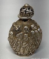 Front view of Tibet silver snuff bottle showing raised monk designs and pierced cap.