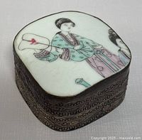 View of the vintage Chinese hand painted porcelain and metal pill box showing the porcelain lid with traditional Chinese figure and metal embossed patterned base.