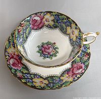Top-down view of teacup and saucer set showing detailed floral mosaic pattern and gold trim.