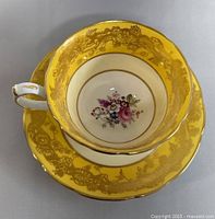 Top view of yellow and gold floral vintage Hammersley teacup with central floral flowers inside, sitting on matching saucer.