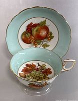 Close-up of the saucer with apple and berry design, light blue rim, and gold trim visible.