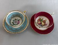 Two vintage English teacup and saucer sets; left is Paragon teacup with turquoise and gold floral design, right is English Windsor teacup with realistic fruit interior and red exterior, matching saucer visible under Windsor teacup.