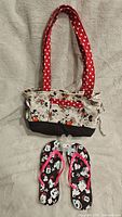 Full view of the Minnie Mouse themed flip flops under the Minnie Mouse themed shoulder bag with red polka dot handles