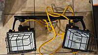 Top view of the dual work light setup showing two rectangular lights with reflective backing and protective wire cages mounted on a black metal frame. Yellow cord connected.