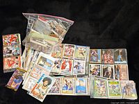 Initial overview showing large assortment of trading cards spread out, some in plastic sleeves and baggies, across football and basketball.