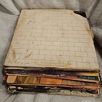 Stack of vinyl records with visible wear and creasing on covers, top record is Pink Floyd's The Wall with a white brick wall design.
