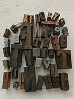 Top view of assorted vintage printing blocks including wooden and metal letter blocks in varied sizes arranged loosely on a surface.