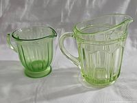 Front view of both Vaseline glass creamers showing difference in size and ribbed design.