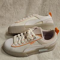 Side profile view of one Puma Mayze sneaker showing white and beige synthetic upper with orange Puma logo stripe and translucent sole.