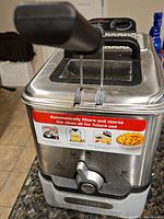 Close-up front and side view of stainless steel T-Fal F58 deep fryer with black handle and red label showing oil filtering instructions.