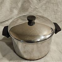 Angled photo of stock pot with lid on showing stainless steel body and black handles.