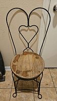 Full view of the chair showing wrought iron backrest with heart shape and round wooden seat with visible wear.