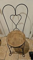Front view of vintage wrought iron chair with a heart-shaped backrest and wooden seat showing wear.