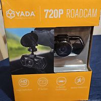 Front of box showing Yada 720P Roadcam dash camera in packaging with lens and mount visible.