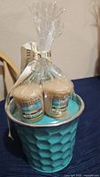 Gift set with two small beige Yankee Candle votive candles in Sun & Sand scent inside turquoise textured container, wrapped in clear plastic with branded ribbon.