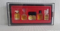 Clear rectangular display case containing five sealed miniature perfume bottles on a red holder. Each bottle is labeled with different Paris perfume names.