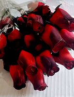 Close-up image of multiple wooden artificial roses showing red petals with black shading, highlighting the detailed petal texture and finish.