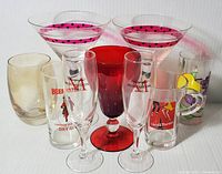 Display of 9 assorted beverage glasses showing variety in color, branding, and style including martini, goblet, flute, and tumbler glasses.