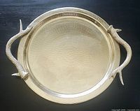 Top-down view of the round hammered metal tray with antler-style handles on black surface.
